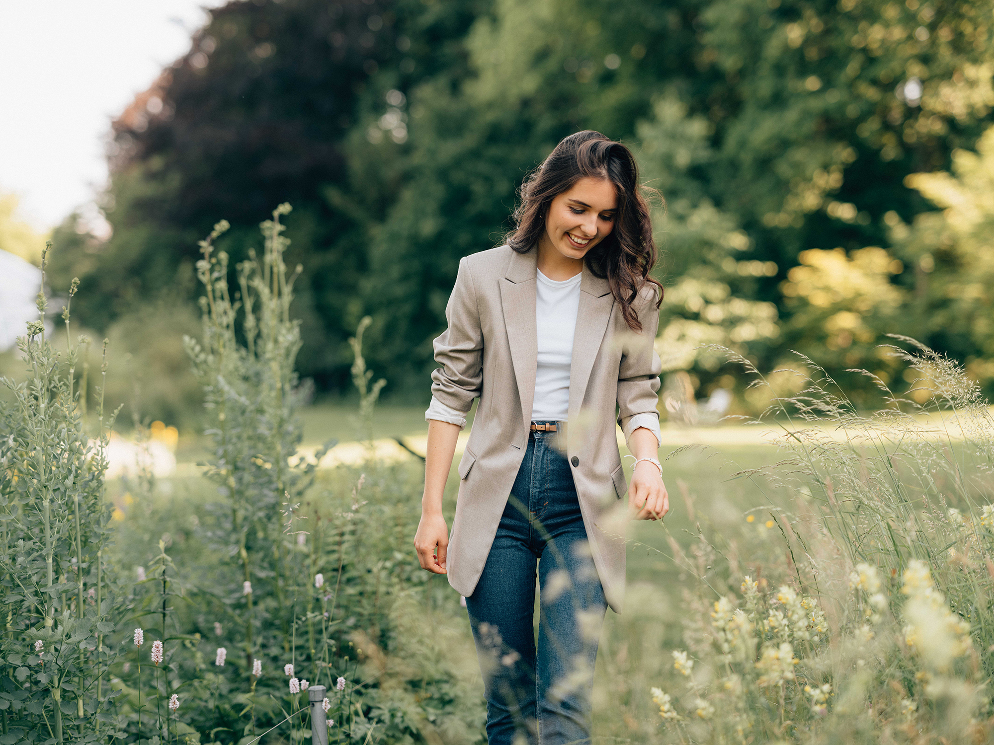 Junge Frau im Blazer geniesst Spaziergang durch hohes Gras