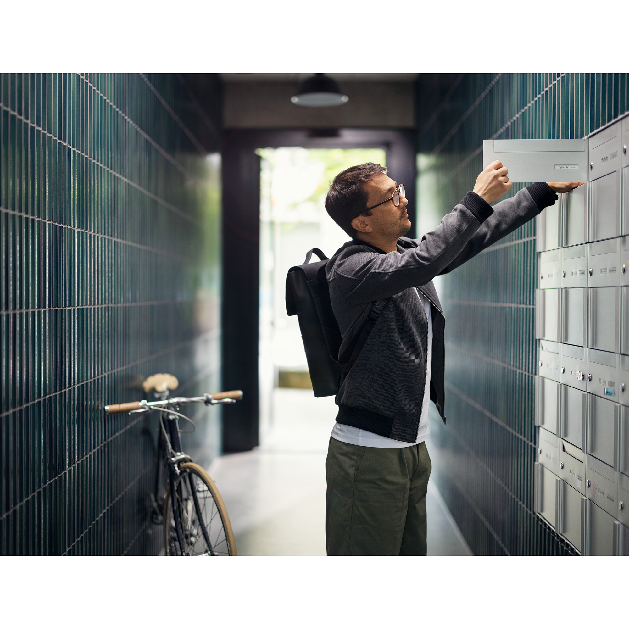 Mann leert Briefkasten im Hauseingang
