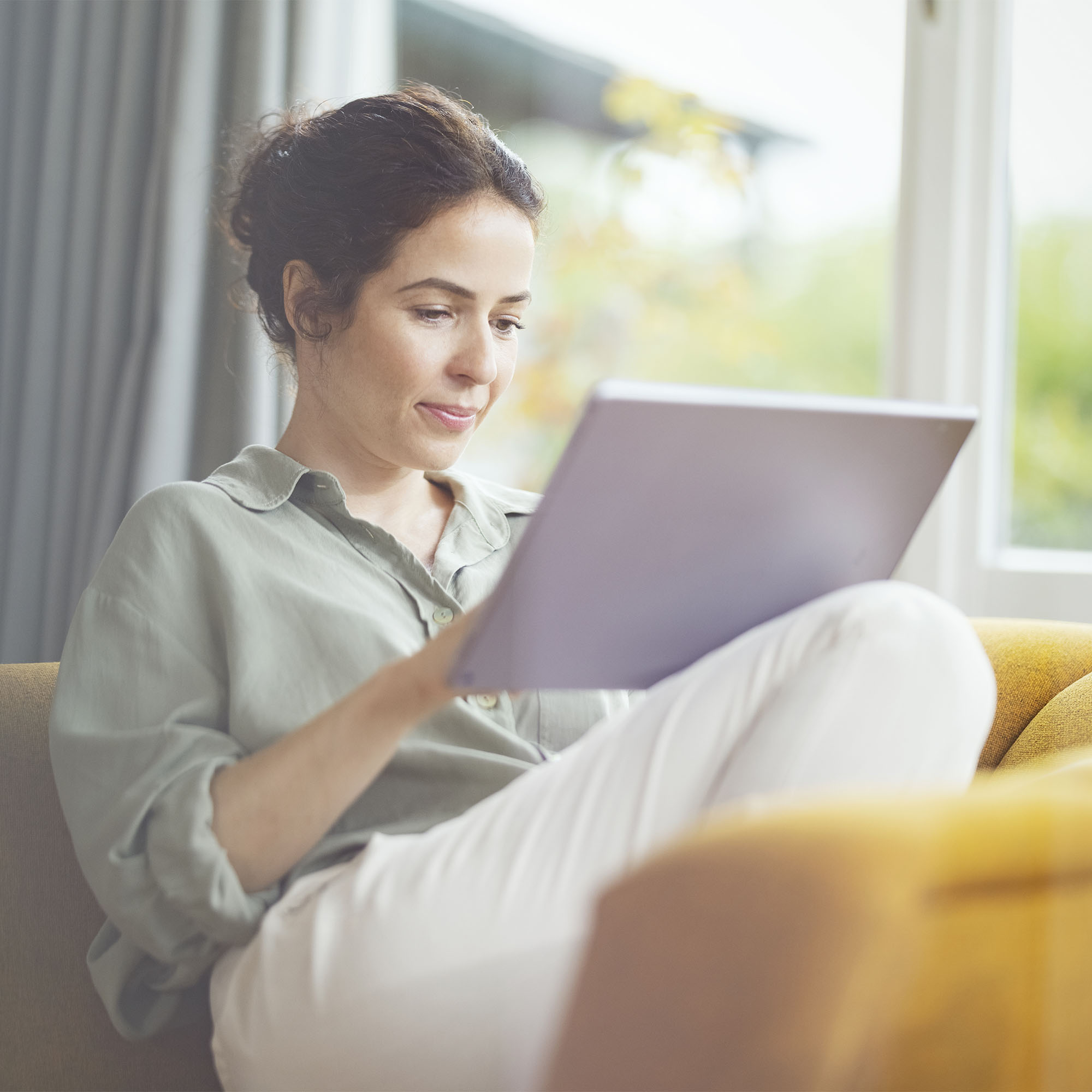 Frau sitzt auf dem Sofa mit Tablet in der Hand