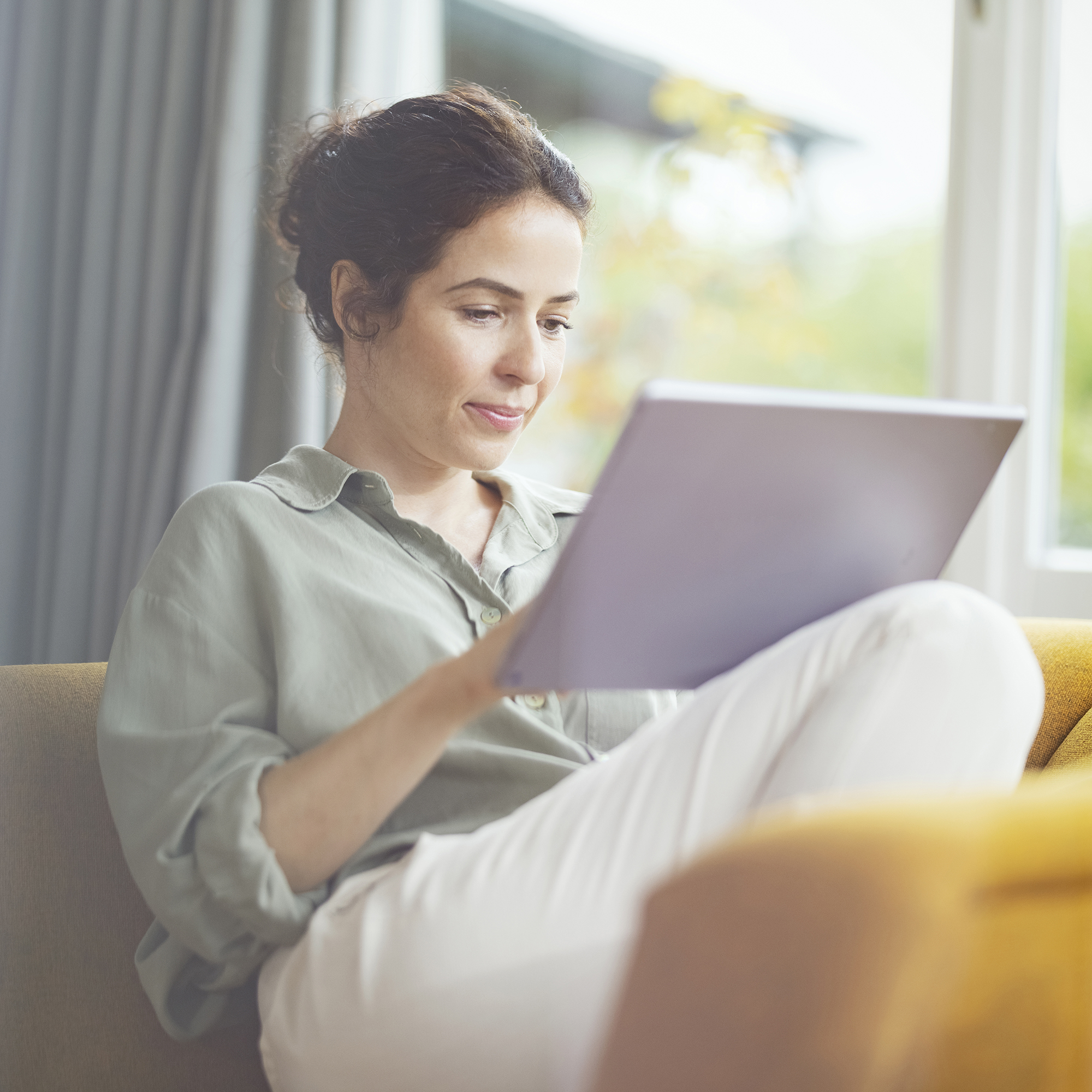 Frau sitzt auf Sofa mit Tablet in der Hand