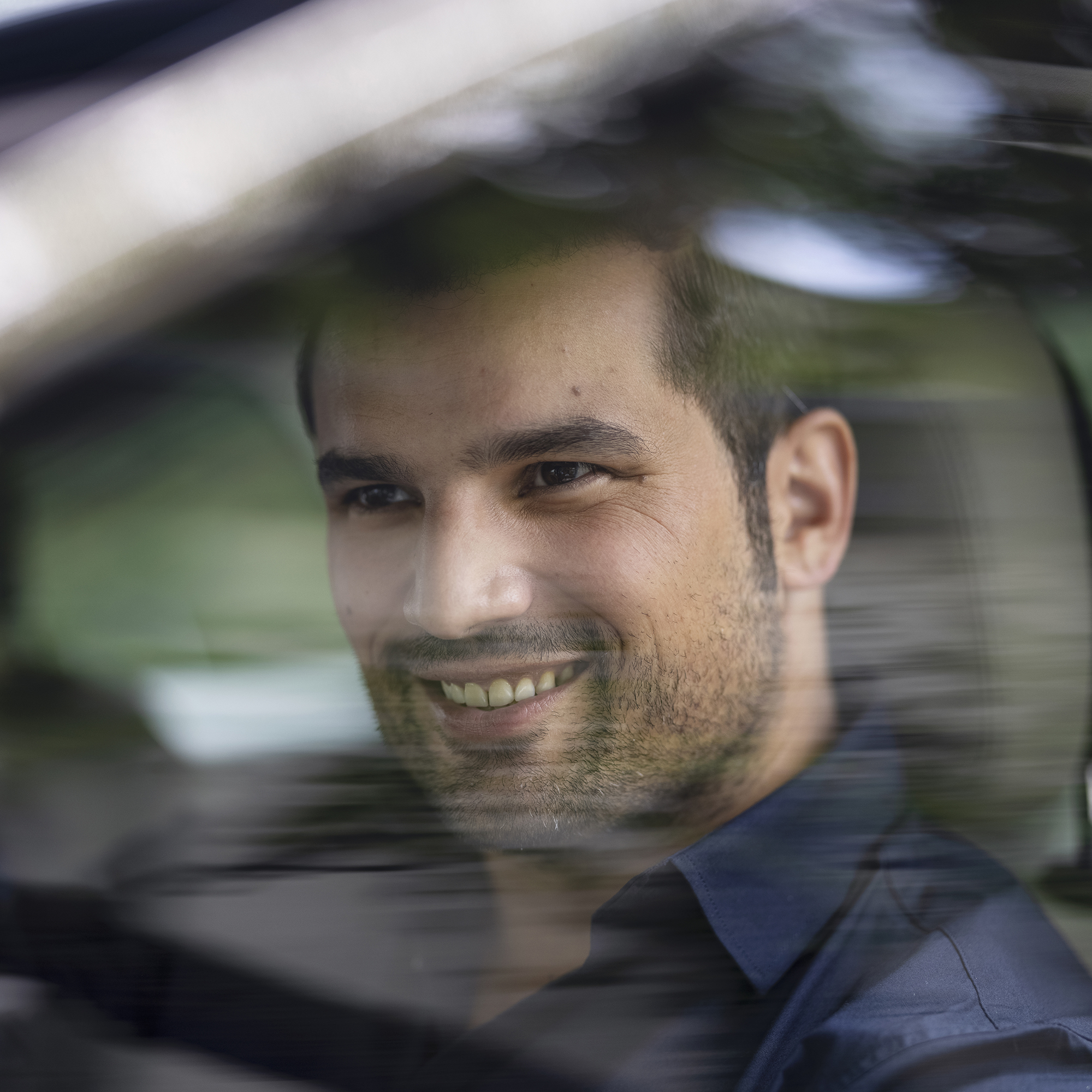Mann sitzt im Auto, hinter reflektierender Scheibe