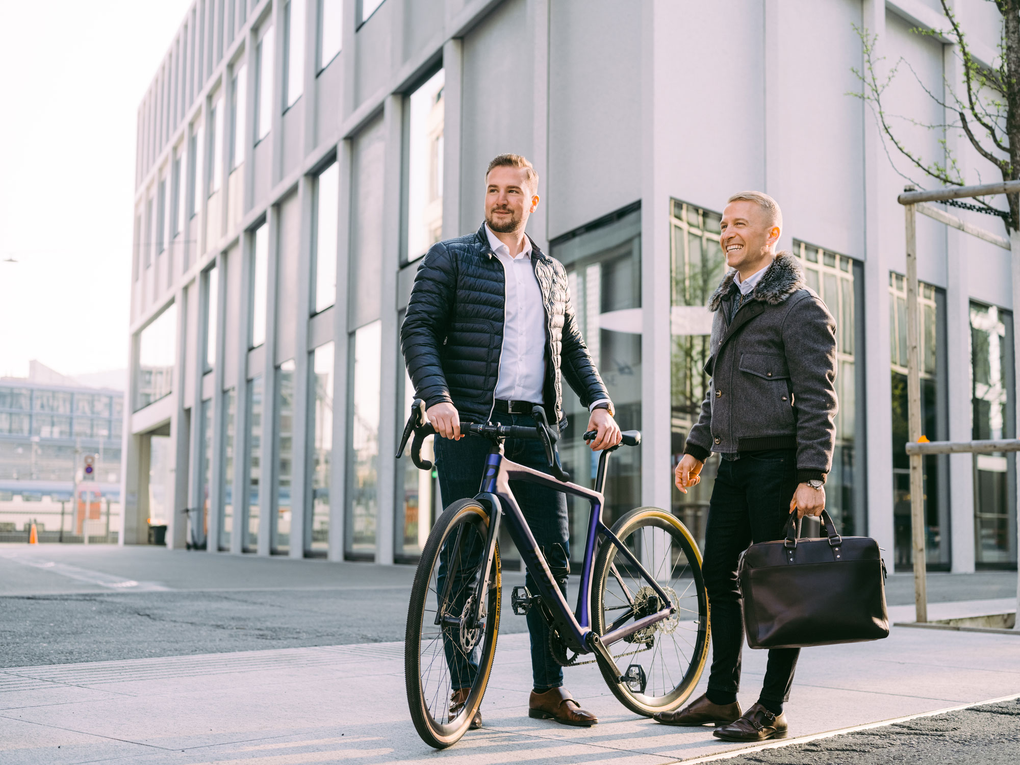 Mitarbeiter mit Velo und Kollege mit Aktentasche treffen sich vor Migros Bank